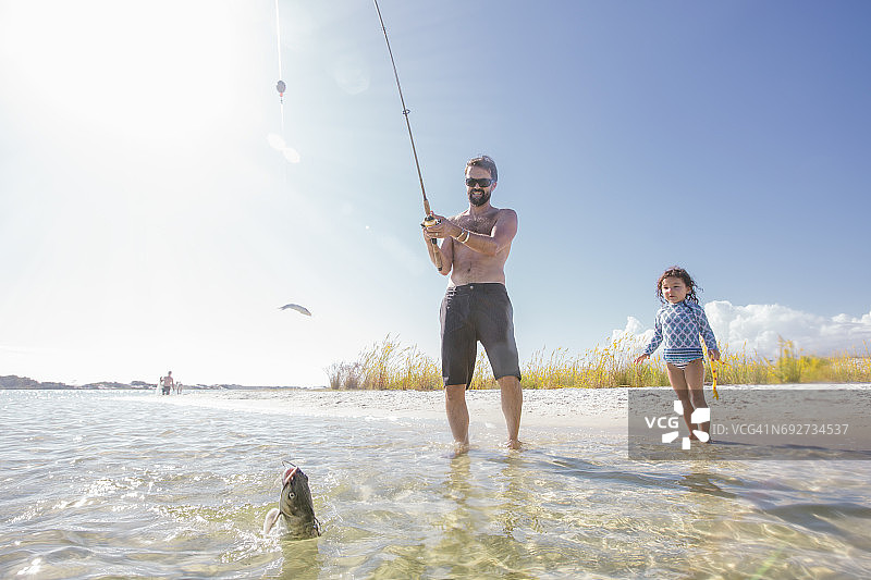 女儿观看父亲在美国佛罗里达州沃尔顿堡海滩捕鱼图片素材