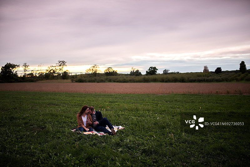 日落时分，浪漫情侣在野餐毯上放松图片素材