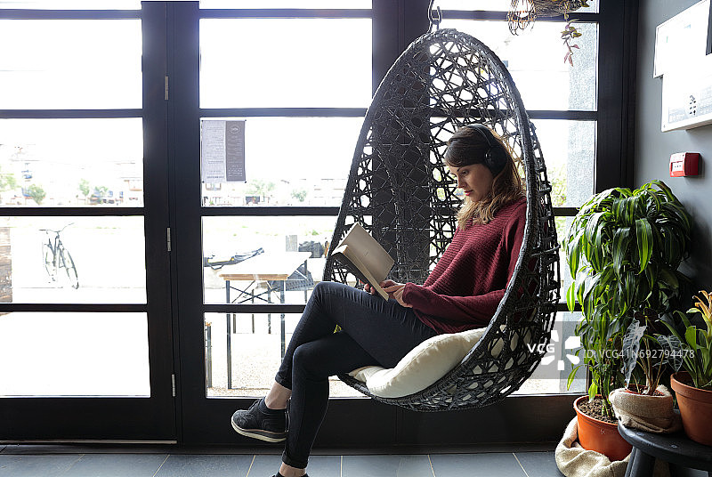 年轻女人在咖啡馆戴着耳机看书图片素材