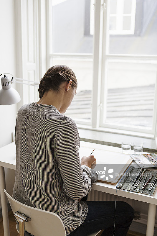在创意办公室里对着窗户在画布上绘画的艺术家的背影图片素材