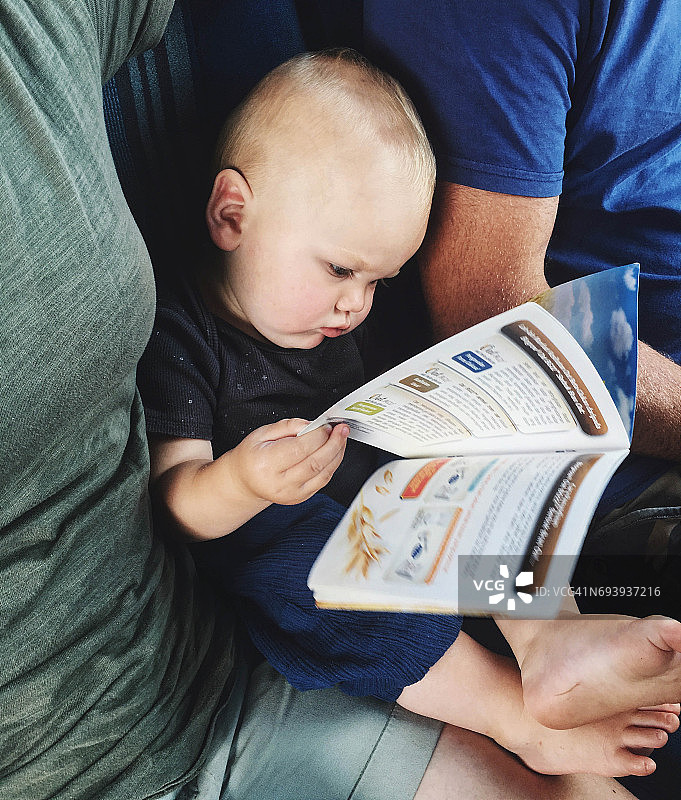 儿童坐在父母中间，专心阅读中文宣传册图片素材