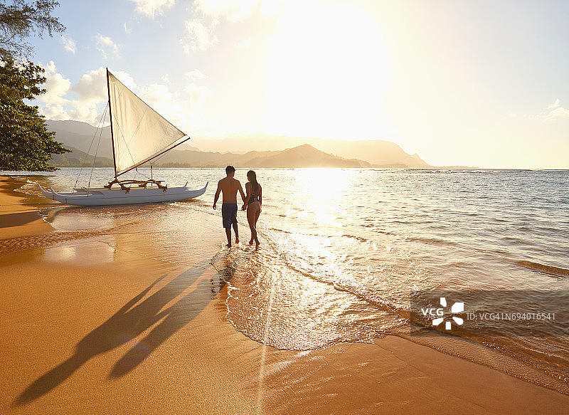 情侣在帆船附近的海滩漫步图片素材