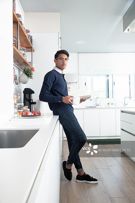 在厨房阅读的年轻印度男人图片素材