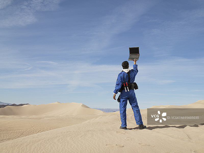 研究员在沙漠中手持笔记本电脑寻找无线连接图片素材