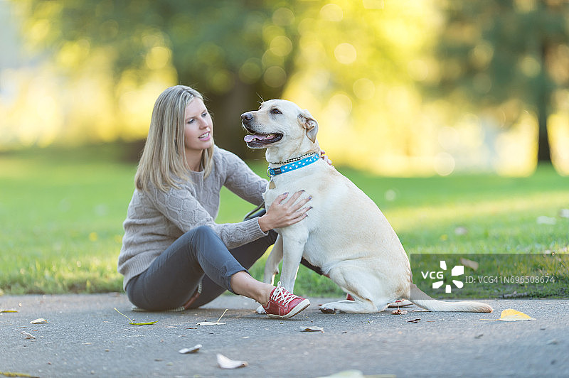 在美丽的夏日傍晚在公园里遛狗的白人妇女图片素材