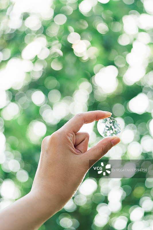 手持放大镜，背景为绿色树木散景图片素材