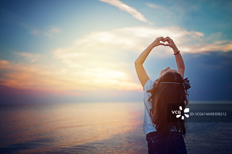 夕阳下用手指比心的小女孩图片素材