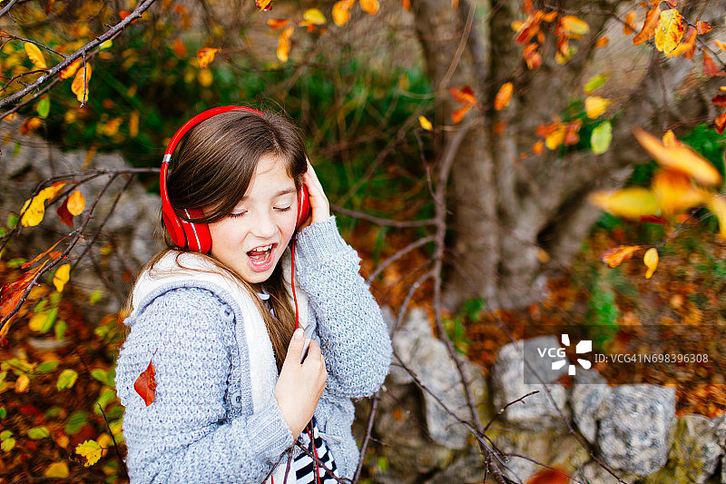 秋天，在色彩鲜艳的树下戴着耳机听音乐的年轻女孩图片素材
