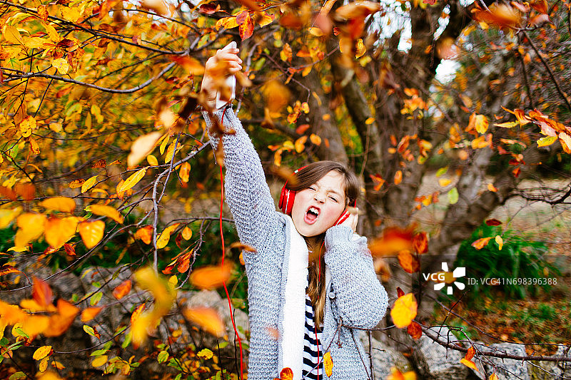 秋天，在色彩鲜艳的树下戴着耳机听音乐的年轻女孩图片素材