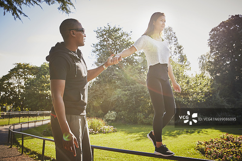 女人与私人教练手牵手在公园栅栏上行走图片素材