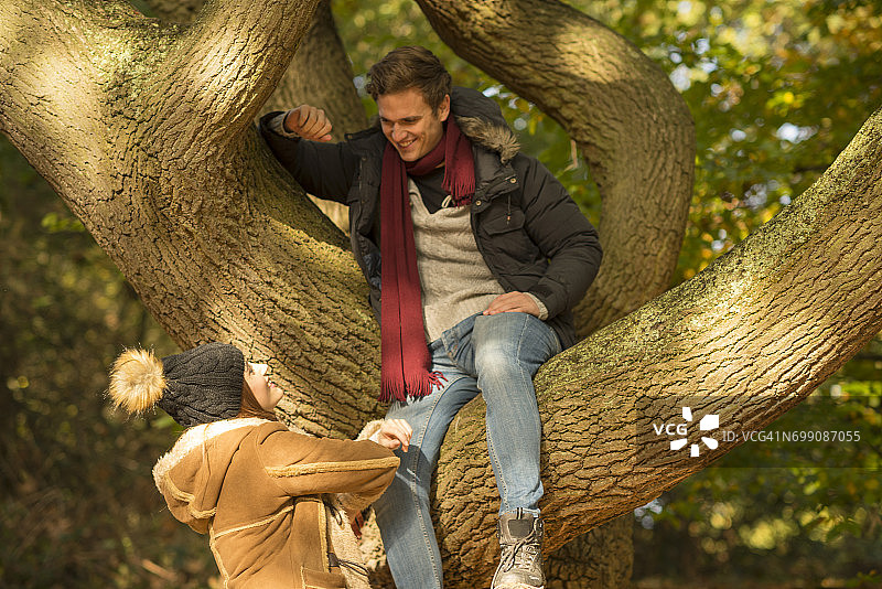 坐在树上，向下看着地面上年轻女人的年轻人图片素材