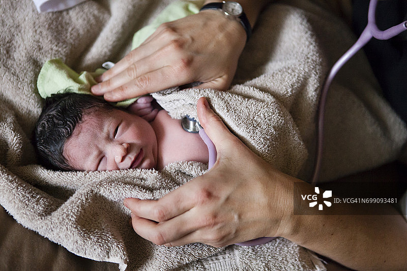 在家中分娩的新生婴儿，助产士在出生后不久检查所有生命体征，这是一项新生儿筛查，她在此检查心率图片素材