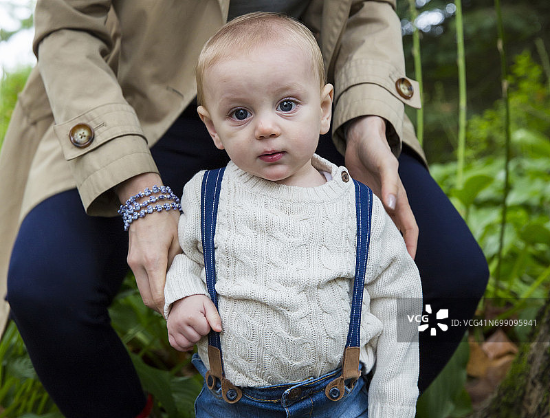 在花园里，可爱的男宝宝在妈妈的帮助下站立图片素材