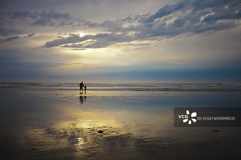 父子在俄勒冈州洛克威海滩度假时观看日落图片素材