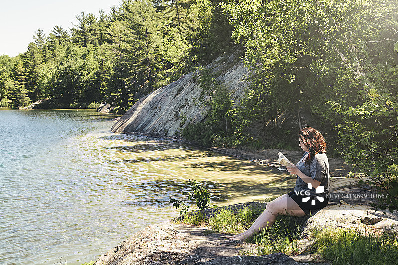 在明媚的夏日，年轻女子在乔治湖岸边平静地读书图片素材