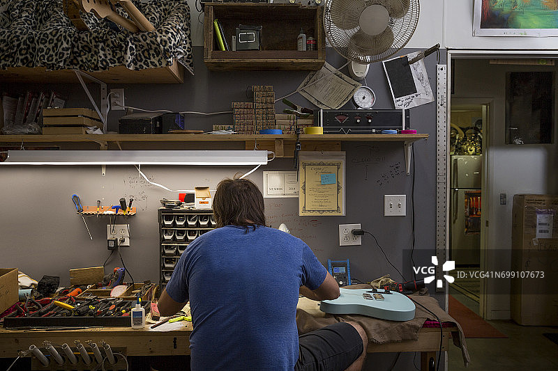 吉他制作师在桌旁制作吉他的后视图图片素材