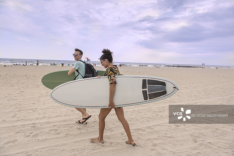 年轻情侣在纽约州洛克威海滩携带冲浪板图片素材