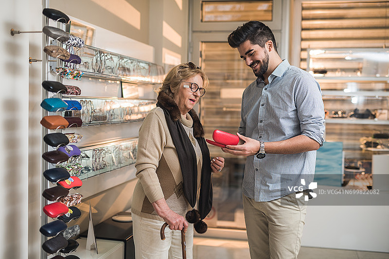 年轻的验光师展示年长妇女的眼镜盒为她的新眼镜。图片素材