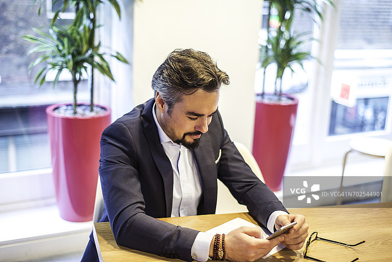 在办公室办公桌旁阅读智能手机短信的商人图片素材