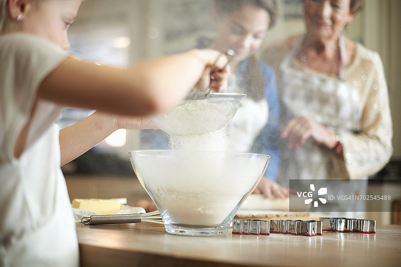 年长的女人和孙女们在为圣诞树饼干筛面粉图片素材