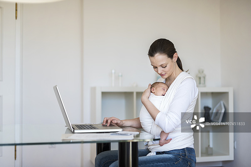 在家工作，用吊带抱着女婴的母亲图片素材