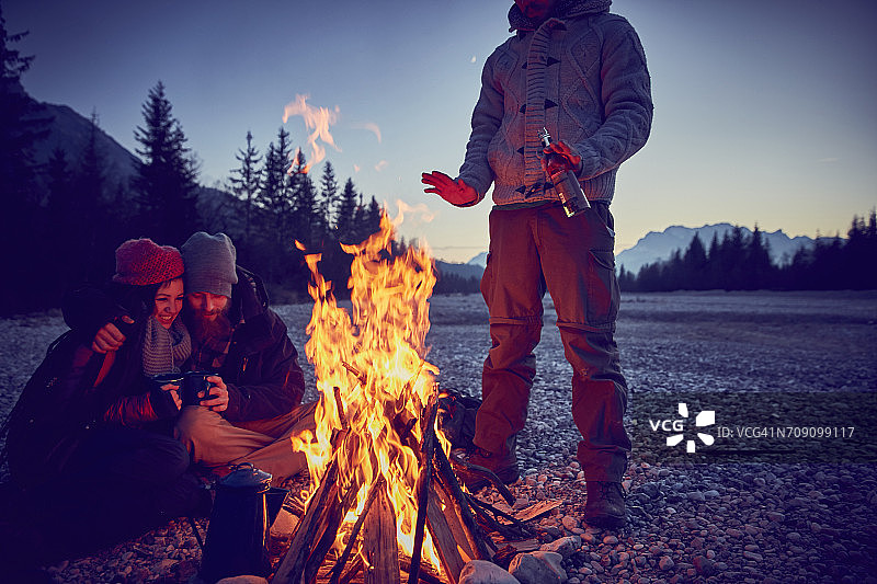 年轻夫妇在伊萨尔河营火旁取暖，背景为德国巴伐利亚州卡尔文德尔山脉图片素材