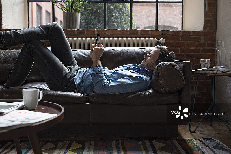 在沙发上使用智能手机的男人图片素材