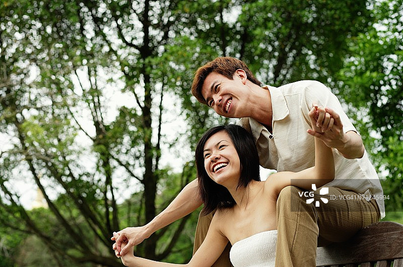 情侣坐在公园长椅上，男人坐在女人身后握着她的手图片素材