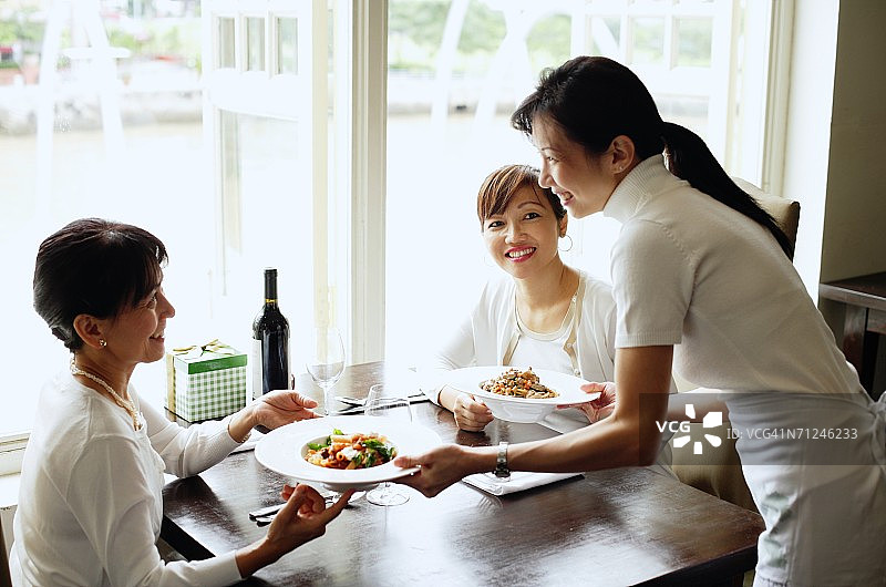 两名女子在餐厅，服务员为她们上菜图片素材