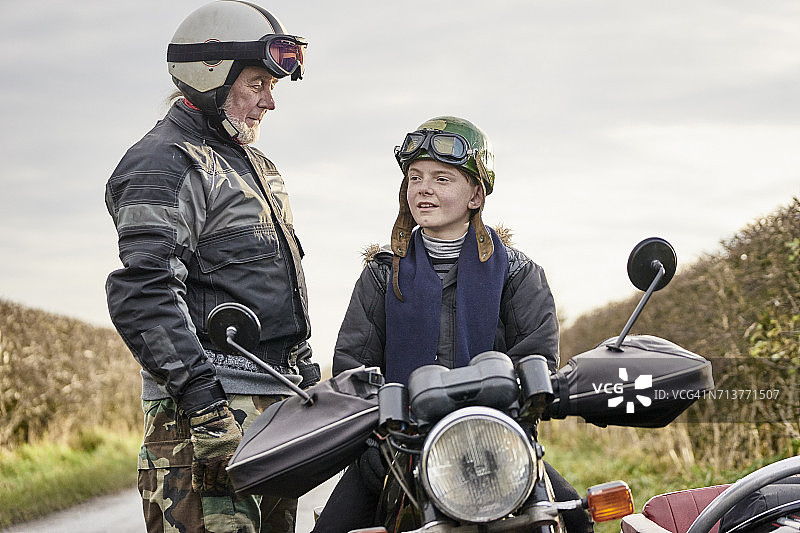 年长的男性摩托车手与坐在摩托车上的孙子交谈图片素材