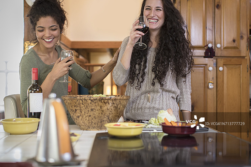 两个女人在厨房柜台准备沙拉并欢笑图片素材
