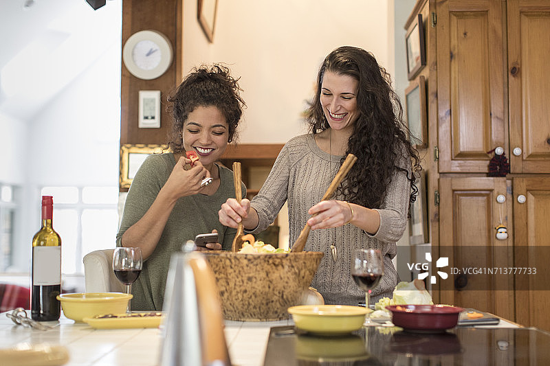两位女性朋友在厨房准备并享用沙拉图片素材
