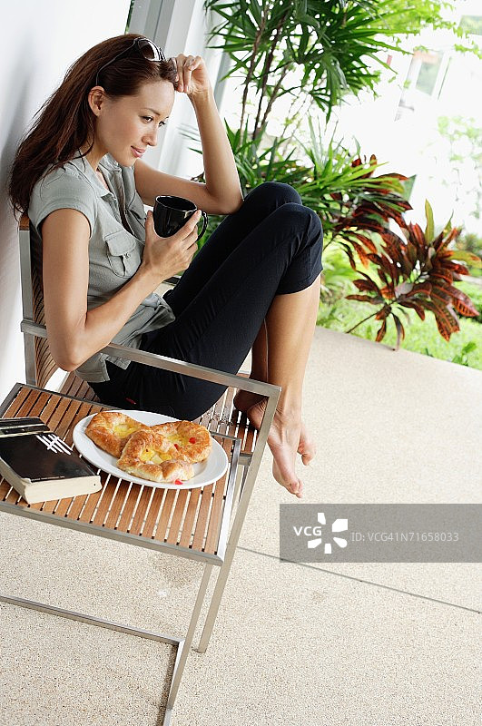 女人在露台上喝咖啡，手放在头上图片素材