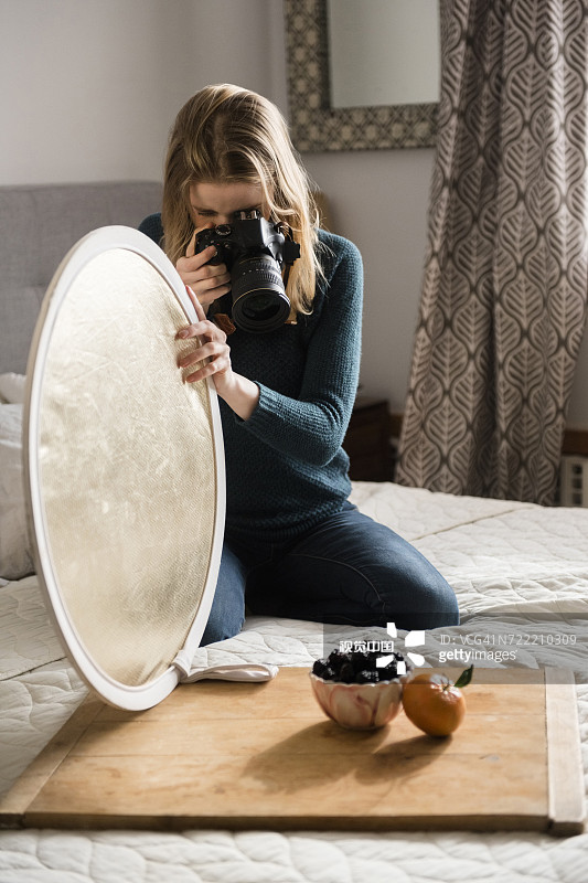 跪在床上举着反光板拍摄水果的女人图片素材