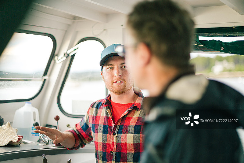 美国缅因州海岸，两名男人在渔船上交谈。图片素材