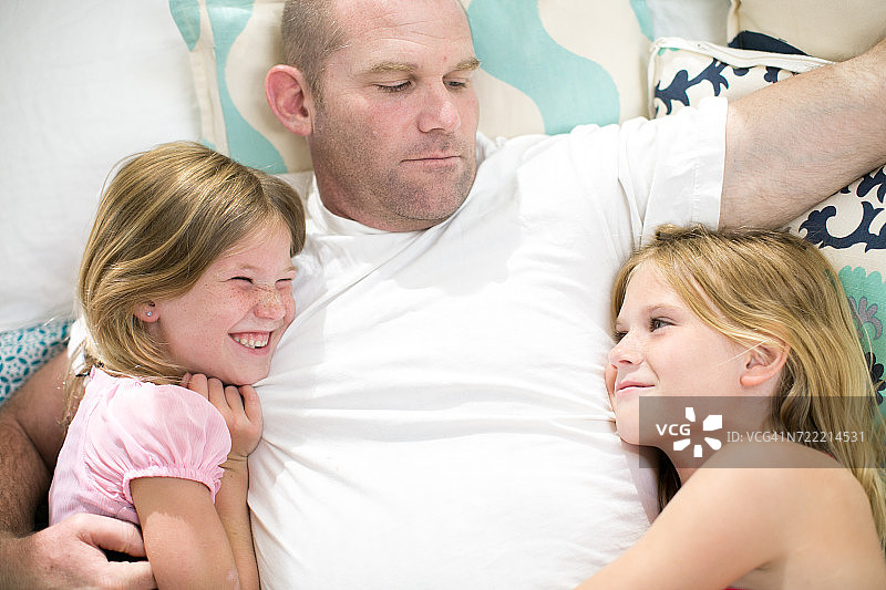 俯视视角：中年男人与两个女儿在床上图片素材