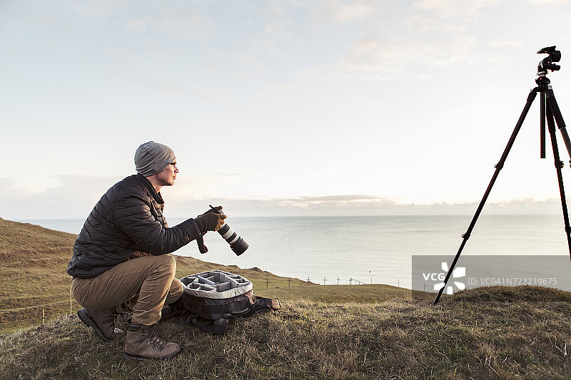徒步旅行者在海边山丘上手持单反相机眺望远方的侧面图图片素材