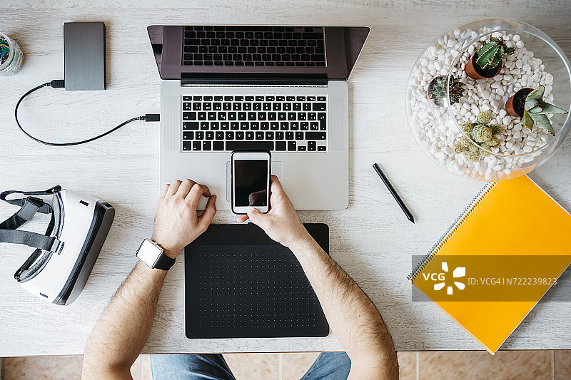 男人在家居办公室使用智能手机和笔记本电脑工作（俯视图）图片素材