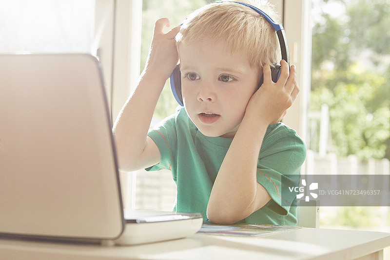男孩在桌前使用笔记本电脑并戴着耳机图片素材