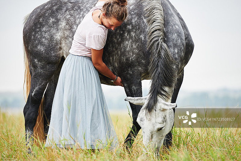 在田野里，手臂搭在灰色斑点马上的裙子女人图片素材