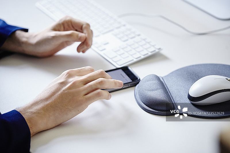 男子坐在桌前使用智能手机和鼠标垫图片素材
