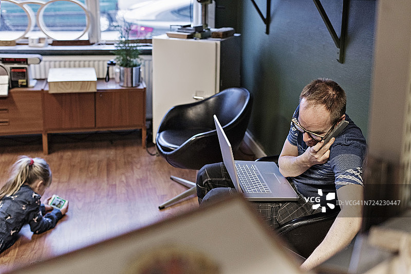 女儿在地板上，店主在眼镜店用智能手机和笔记本电脑俯视图图片素材