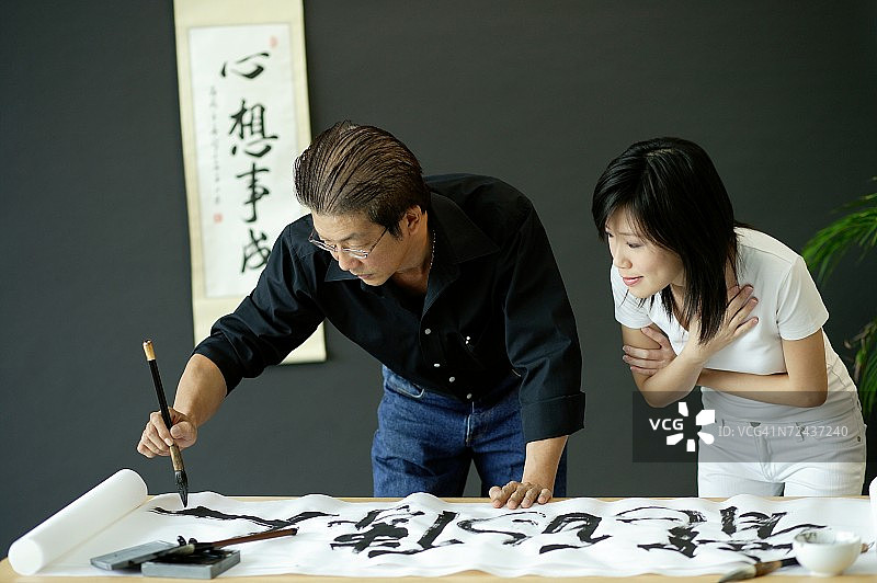 中年男人写中国书法，旁边的女人在观看图片素材