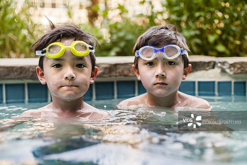 两个男孩戴着泳镜，脸上涂满防晒霜坐在泳池里图片素材