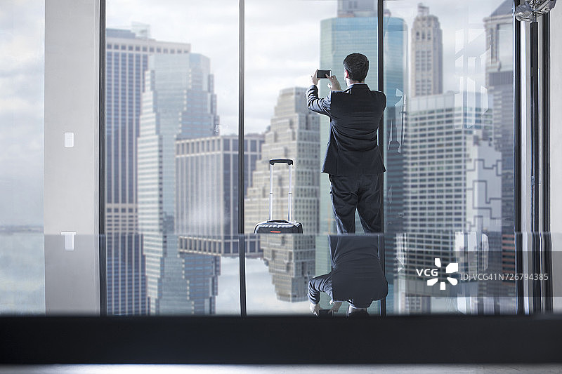 拉着行李箱在办公室拍摄城市景观的商人图片素材