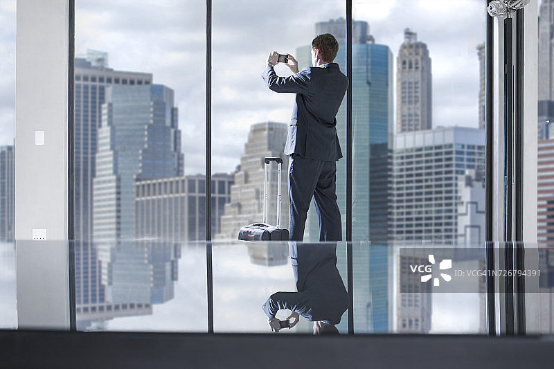 拉着行李箱在办公室拍摄城市景观的商人图片素材