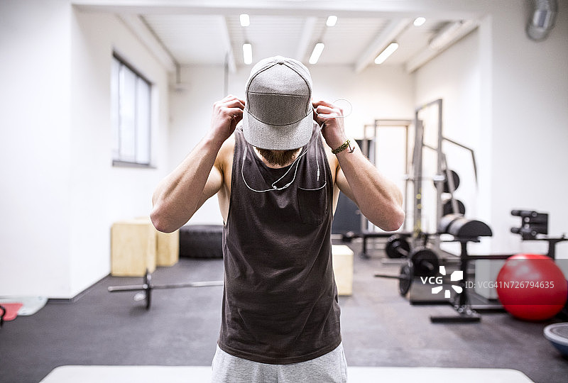 年轻运动员戴着帽子，在健身房里使用耳机图片素材