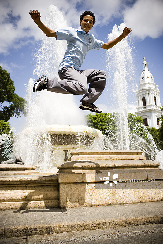 学校男孩在中心广场的喷泉上跳跃图片素材