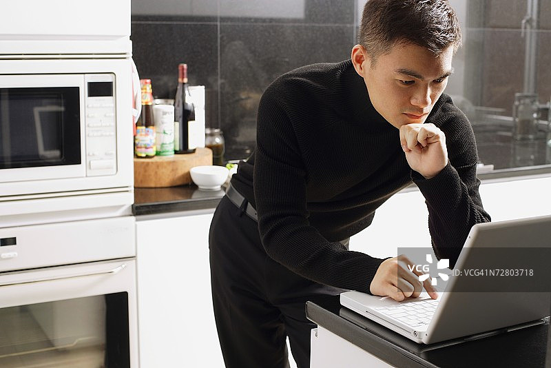 男子在厨房看笔记本电脑图片素材
