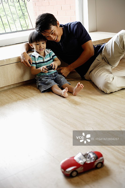 父子坐在家里地板上玩遥控车图片素材